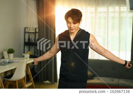 Sporty man exercising with skipping rope, doing domestic training at home. Fitness, sport and healthy lifestyle concept Sporty man exercising with skipping rope, doing domestic training at home. Fitness, sport and healthy lifestyle concept 102667136