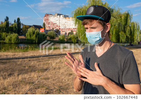 A male blogger in a medical mask in a park filming a video blog on camera. A male blogger in a medical mask in a park filming a video blog on camera. 102667448
