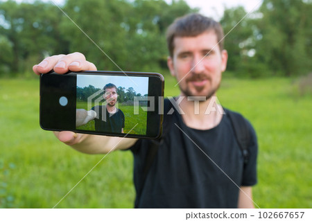A young man is recording a video blog in the park on the phone A young man is recording a video blog in the park on the phone 102667657