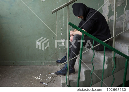 An addict in crisis is sitting on a staircase in an abandoned house. Addiction concept 102668280