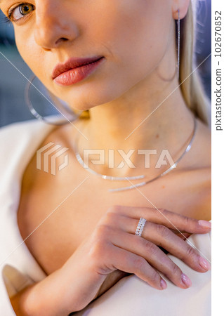 Pretty beautiful girl adorned with a diamond necklace, earrings, and a diamond ring on her finger in a high-end jewelry boutique. 102670852