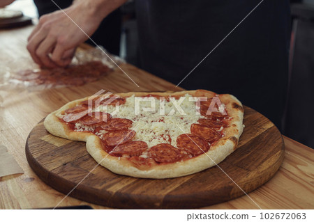 Male hands preparing pizza in the shape of a heart for a romantic gift Male hands preparing pizza in the shape of a heart for a romantic gift 102672063