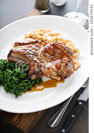 Grilled pork chop with cassoulet and braised greens 102674542