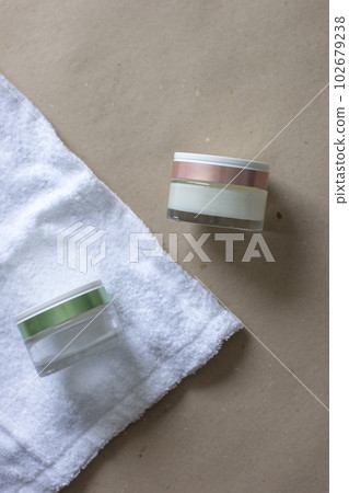 Two glass cosmetic jars with green and pink lid on towel and beige background 102679238