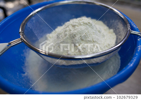 Sifting white flour through a sieve 102679329