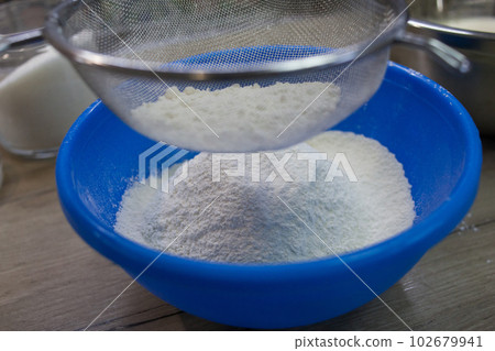 Sifting white flour through a sieve 102679941