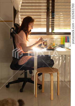 An adult woman having a breakfast at the kitchen table 102681700