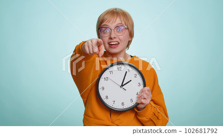Woman showing time on wall office clock, ok, thumb up, approve, pointing finger at camera, your time 102681792