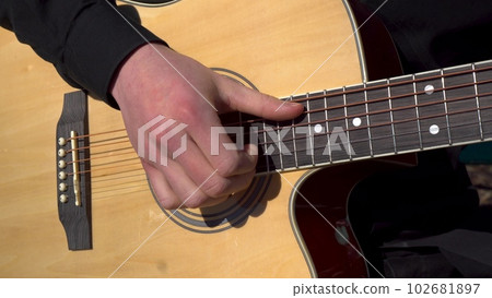 A young man plays the acoustic guitar. Close-up of a hand striking a string. 102681897