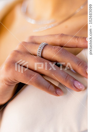 Girl's hand adorned with a beautiful and expensive diamond ring. Stylish high-end diamond bracelet on girl's wrist, touching the collar of her jacket in a gold and jewelry boutique. 102683099