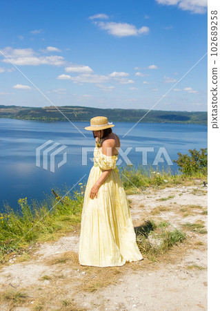 A girl in a long dress standing on a cliff by the bay 102689258