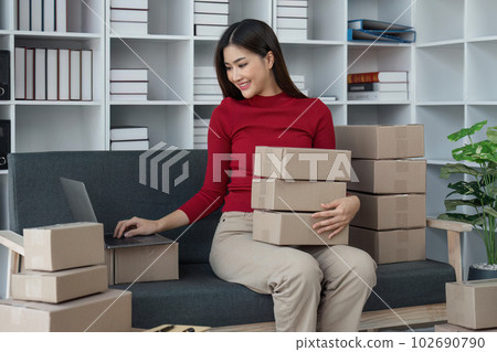 Female seller write the customer's address on the parcel box to prepare for delivery and using laptop checking day's sales on the online store, Concept of parcel delivery and selling online Female seller write the customer's address on the parcel box to prepare for delivery and using laptop checking day's sales on the online store, Concept of parcel delivery and selling online 102690790