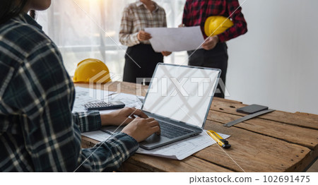 Team of structural engineers working in office looking at laptop discussing design of building plan 102691475