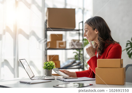 Female online seller preparing delivery items and using calculator to calculate orders Female online seller preparing delivery items and using calculator to calculate orders 102691550