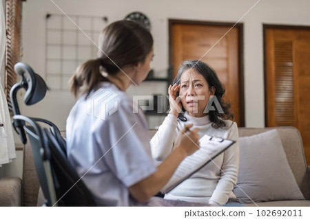 Female doctor is examining elderly patient while taking notes of illness. Patient is having headache. Health care concept 102692011