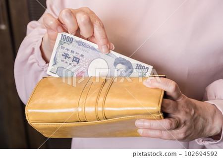 [Housewife taking out a 1000 yen bill from a long wallet] 102694592