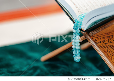 Holy Quran with prayer rosary beads on wooden stand 102694746