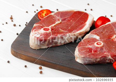 Raw lamb steak on board on white wooden table Raw lamb steak on board on white wooden table 102696935