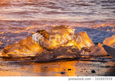 Icebergs Shining on Black Volcanic Sand at Sunset. Clear Ice Crashed by Ocean Waves. Famous Tourist Location in North Europe Country. Diamond Beach in Iceland. Travel Destination. High Resolution. 102697059
