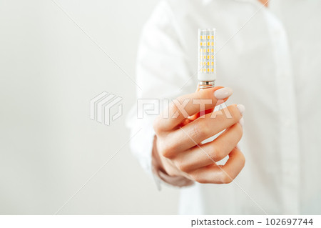 Woman in white shirt holding light bulb in hand Woman in white shirt holding light bulb in hand 102697744