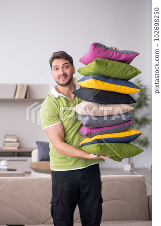 Young man with a lot of pillows sitting on the sofa Young man with a lot of pillows sitting on the sofa 102698250