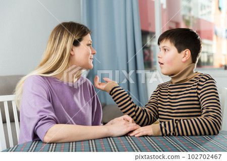Portrait of young woman and son chatting at table Portrait of young woman and son chatting at table 102702467