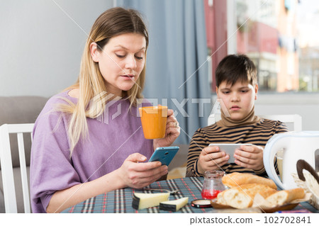 Portrait of young mother and son using phones during breakfast 102702841