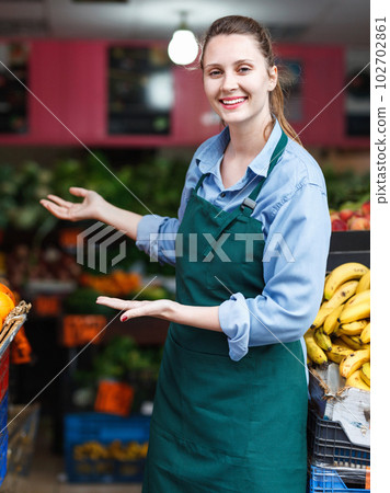 Seller woman is standing near shoecase with vegetables and fruits on the workplace in the market. Seller woman is standing near shoecase with vegetables and fruits on the workplace in the market. 102702861