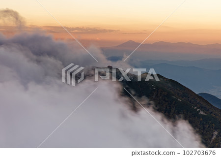 A distant view of Mt. Hinokio and Mt. Tateshina at dusk with clouds flowing from Mt. A distant view of Mt. Hinokio and Mt. Tateshina at dusk with clouds flowing from Mt. 102703676