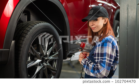 Woman mechanic uses pneumatic wrench to tighten the wheel nut. Girl at men's work. Woman mechanic uses pneumatic wrench to tighten the wheel nut. Girl at men's work. 102704470