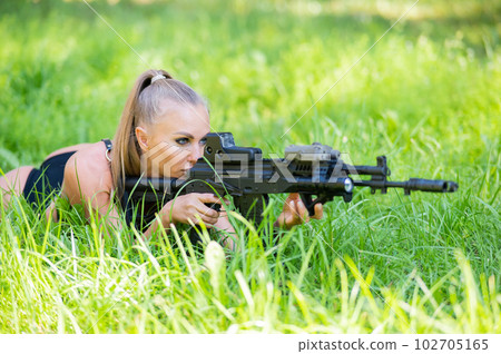 Caucasian woman in bikini lies with machine gun on green grass. Caucasian woman in bikini lies with machine gun on green grass. 102705165