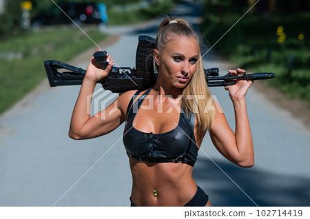 Caucasian woman in bikini with machine gun outdoors. 102714419
