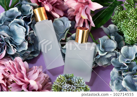 Two frosted glass cosmetic bottles surrounded by flowers Two frosted glass cosmetic bottles surrounded by flowers 102714555