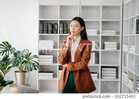 Young attractive Asian female office worker business suits smiling at camera in modern office . Young attractive Asian female office worker business suits smiling at camera in modern office . 102715401