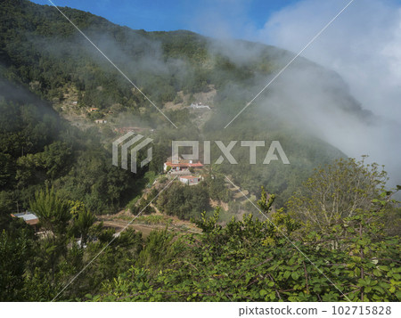 View of small village El Cedro, foggy green hill at mist laurisilva forest of the Garajonay National Park. Hiking trail at La Gomera, Canary Islands, Spain. 102715828