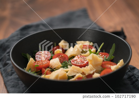 Fresh salad with cherry tomatoes, arugula and hard vintage cheese in black bowl on linen napkin Fresh salad with cherry tomatoes, arugula and hard vintage cheese in black bowl on linen napkin 102717190