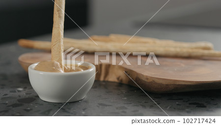man hand dip grissini in cashew paste in white bowl on terrazzo countertop 102717424