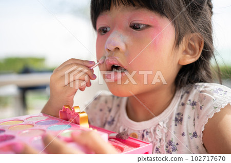 Adorable little child Asian girl paints her mouth with pink children heads and looks in the mirror. A child plays at home in a toy beauty salon. Increase learning development for preschoolers. Adorable little child Asian girl paints her mouth with pink children heads and looks in the mirror. A child plays at home in a toy beauty salon. Increase learning development for preschoolers. 102717670