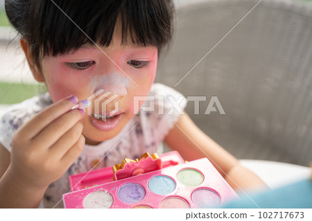 Adorable little child Asian girl paints her mouth with pink children heads and looks in the mirror. A child plays at home in a toy beauty salon. Increase learning development for preschoolers. 102717673
