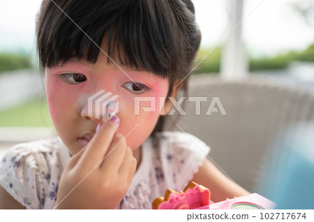 Adorable little child Asian girl paints her mouth with pink children heads and looks in the mirror. A child plays at home in a toy beauty salon. Increase learning development for preschoolers. 102717674