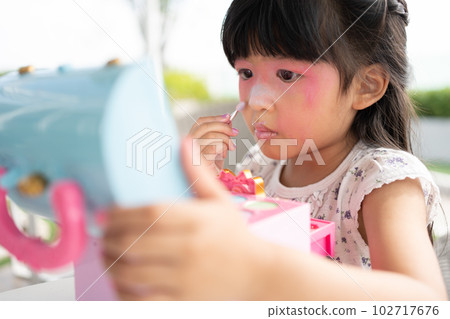 Adorable little child Asian girl paints her mouth with pink children heads and looks in the mirror. A child plays at home in a toy beauty salon. Increase learning development for preschoolers. Adorable little child Asian girl paints her mouth with pink children heads and looks in the mirror. A child plays at home in a toy beauty salon. Increase learning development for preschoolers. 102717676