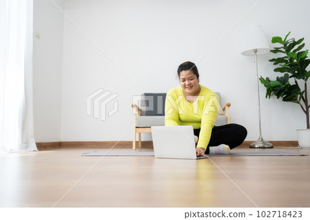 Asian overweight woman doing stretching exercise at home on fitness mat. Home activity training, online fitness class. Stretching training workout on yoga mat at home for good health and body shape. 102718423