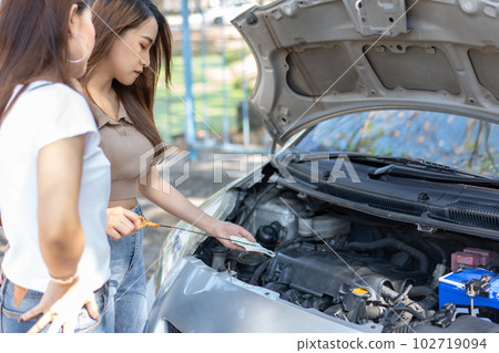 Two Asian people try to check the car engine and wait for assistance after a car breakdown on street. Concept of a vehicle engine problem or accident and emergency help from a Professional mechanic 102719094