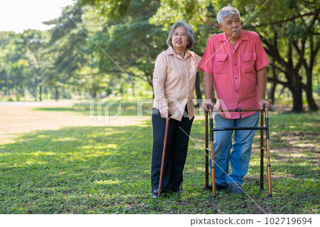 An old elderly Asian man uses a walker and walks in the park with his wife.  Concept of happy retirement With Love and care from family and caregiver, Savings, and senior health insurance 102719694