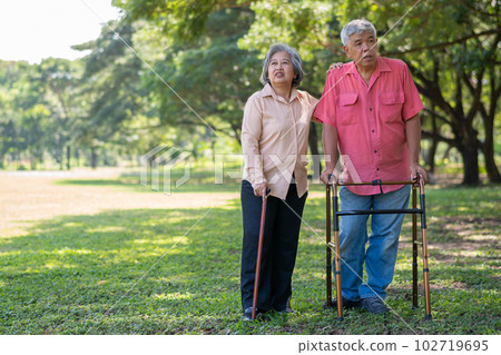 An old elderly Asian man uses a walker and walks in the park with his wife. Concept of happy retirement With Love and care from family and caregiver, Savings, and senior health insurance An old elderly Asian man uses a walker and walks in the park with his wife. Concept of happy retirement With Love and care from family and caregiver, Savings, and senior health insurance 102719695
