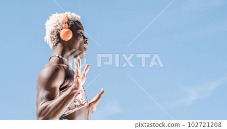 Transgender person dancing while listening to music with headphones outdoors. 102721208