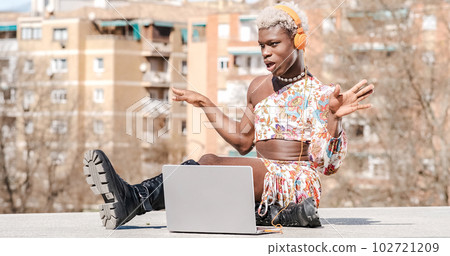 Positive black transgender person typing on laptop on stairs 102721209