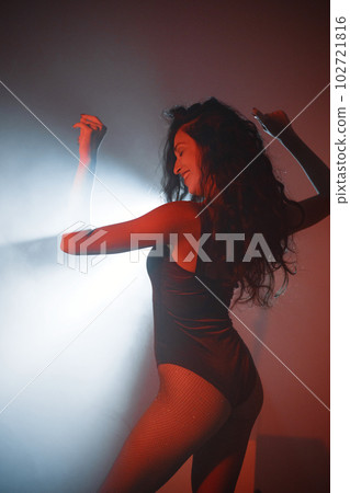 Young curly brunette girl posing for a photo. Girl wearing red velour bodysuit. Projectors light girl up. 102721816