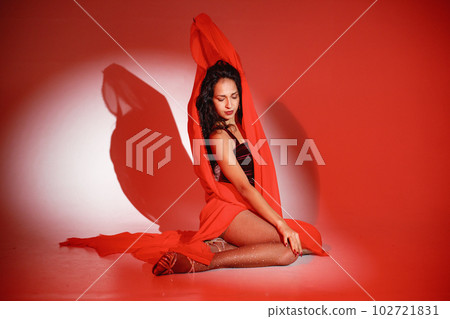 Curly brunette girl posing for a photo. Girl wearing velour bodysuit and is wrapped in red scarf. Projectors light girl up. 102721831