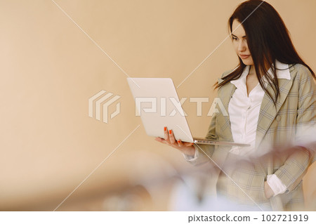Woman in a studio. Lady with a laptop. Brunette in a brown jacket. 102721919